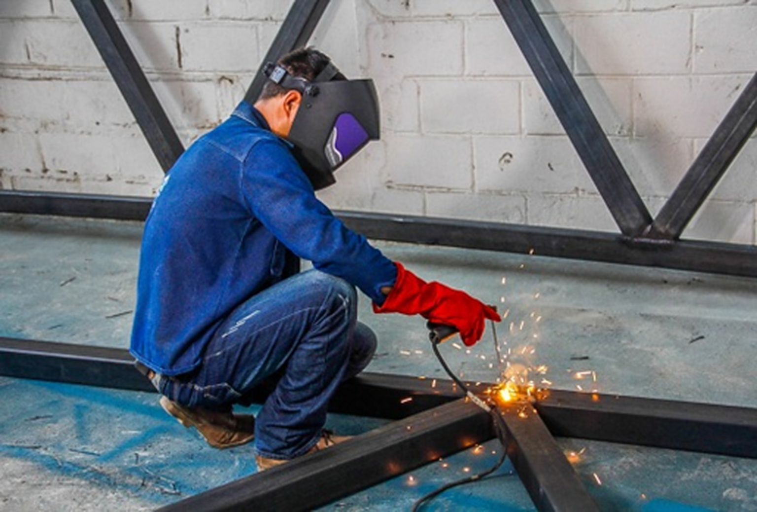 Operario con equipo de protección realizando soldadura en una estructura metálica.